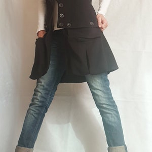 May include: A black vest with a large, folded collar, worn over a white shirt and blue jeans. The vest has a double-breasted closure with buttons and a skirt-like bottom.