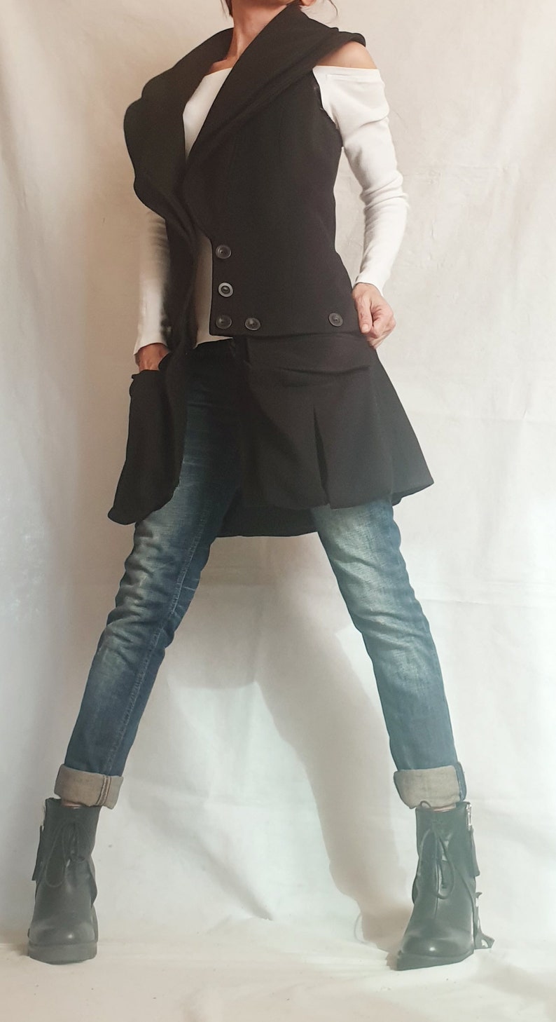 May include: A black vest with a large, folded collar, worn over a white shirt and blue jeans. The vest has a double-breasted closure with buttons and a skirt-like bottom.