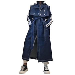 May include: A long dark blue denim trench coat featuring a double-breasted front with white buttons, a matching tie belt at the waist, and prominent white vertical stripes running down the length of the sleeves. The coat has a wide collar.