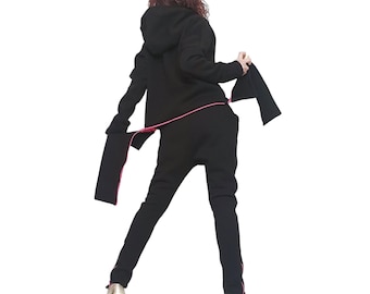 Puede incluir: Una sudadera negra con capucha y pantalones negros a juego con ribetes de color rosa brillante a lo largo de las costuras y bordes. La sudadera incluye capucha y mangas largas, mientras que el pantalón es de corte ajustado. Zapatos dorados.