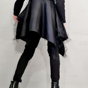 May include: Black long-sleeved top with a flared, asymmetrical skirt. The skirt has a satin-like appearance and is trimmed with a delicate, sheer fabric. The outfit is paired with black pants and black ankle boots with zippers.