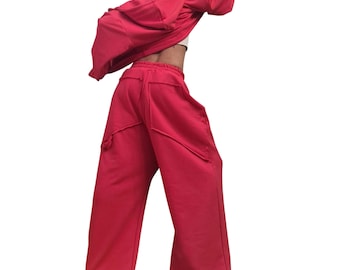 Peut inclure: Un ensemble assorti rouge vif composé d'une veste à capuche zippée et d'un pantalon de jogging large. Le pantalon présente une taille haute avec des coutures horizontales marquées au niveau des hanches et une coupe ample sur les jambes.
