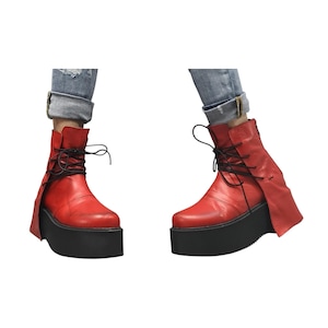 K&ouml;nnte beinhalten: Rote Leder-Ankle Boots mit schwarzen Plateausohlen und schwarzen Schn&uuml;rsenkeln. Die Stiefel haben ein einzigartiges Design mit einer Klappe an der Seite. Die Stiefel werden mit blauen Jeans getragen.