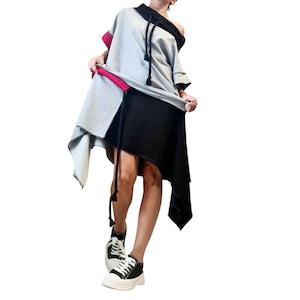 Puede incluir: Vestido asimétrico gris, negro y blanco. La parte superior es gris con cuello negro y ribete rojo. La falda es negra y tiene un dobladillo irregular. El conjunto se completa con zapatillas deportivas blancas y negras.