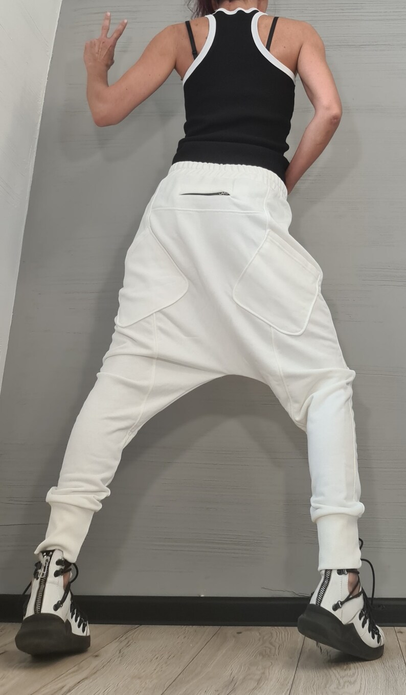 Op de afbeelding: Witte broek met lage kruis met grote zakken en een zwart ritsdetail. De broek wordt gecombineerd met een zwarte tanktop met witte bies en zwart-witte sneakers. De outfit heeft een moderne, stijlvolle uitstraling.