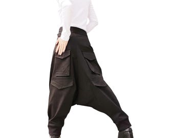 May include: Black harem trousers featuring multiple cargo pockets. The trousers have a relaxed fit and are worn with black heeled boots. The model is wearing a white long-sleeved top.
