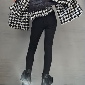 May include: A black and white houndstooth jacket with a quilted black center panel, paired with solid black leggings and black ankle boots featuring a block heel and side buckle detail. The jacket has a wide collar and long, loose sleeves.