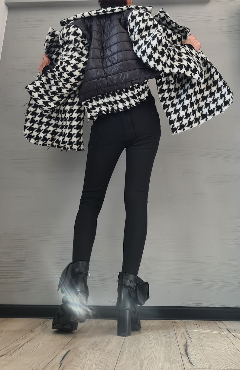 May include: A black and white houndstooth jacket with a quilted black center panel, paired with solid black leggings and black ankle boots featuring a block heel and side buckle detail. The jacket has a wide collar and long, loose sleeves.