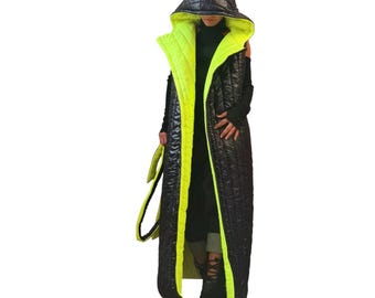 May include: A long, sleeveless, quilted puffer vest featuring a black exterior and a vibrant neon yellow interior lining. The garment includes an oversized, pointed hood and a matching tie belt, showcasing a high-contrast color scheme throughout.