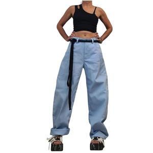 May include: A black sleeveless top with an asymmetrical cutout neckline paired with light blue wide-leg trousers featuring a high waist, a black rope belt, and large side pockets. The outfit is completed with white platform sandals with black soles.