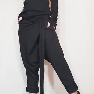 May include: Black ensemble featuring a turtleneck top with cut-out shoulders and long sleeves with fingerless gloves. The outfit includes loose-fitting pants with a long tie and black ankle boots. The overall style is modern and edgy.