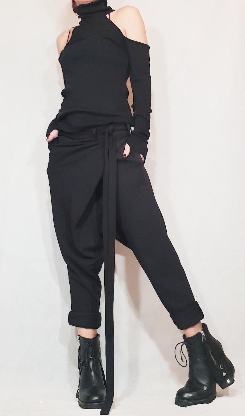 May include: Black ensemble featuring a turtleneck top with cut-out shoulders and long sleeves with fingerless gloves. The outfit includes loose-fitting pants with a long tie and black ankle boots. The overall style is modern and edgy.