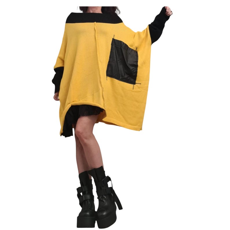 May include: An oversized yellow sweater featuring a wide black ribbed neckline, long black sleeves, and a large black rectangular pocket on the front. The garment has a loose, boxy fit with visible seam detailing and is paired with black platform boots.