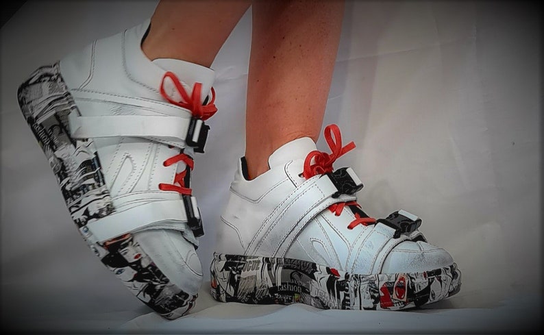 Pu&ograve; includere: Sneakers bianche con plateau, lacci rossi e fibbie nere. Le suole e i lati delle scarpe sono decorate con una stampa grafica in bianco e nero. Scarpe uniche.