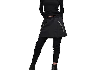 Puede incluir: Conjunto negro que incluye un top con hombros descubiertos y mangas largas, una falda-pantalón con bolsillos con cremallera, leggings negros y botines. El conjunto es completamente negro.