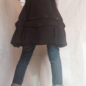 May include: A black vest with a large collar and a ruffled hem. The vest is worn over a white shirt and blue jeans. The person is wearing black boots with zippers on the sides.