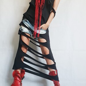 May include: Black, asymmetrical dress with cut-out details and a red fringe necklace. The dress is paired with denim shorts and red leather ankle boots with zippers.