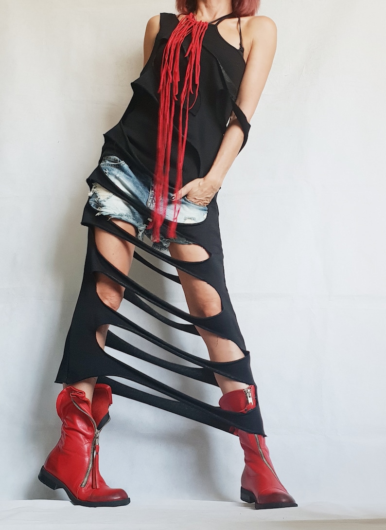 May include: Black, asymmetrical dress with cut-out details and a red fringe necklace. The dress is paired with denim shorts and red leather ankle boots with zippers.