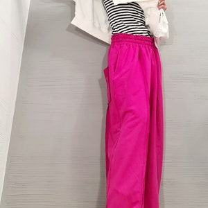 May include: A person wearing a white hooded sweatshirt over a black and white striped top and bright pink sweatpants. The sweatpants have pockets and a drawstring waist. The outfit is casual and comfortable.