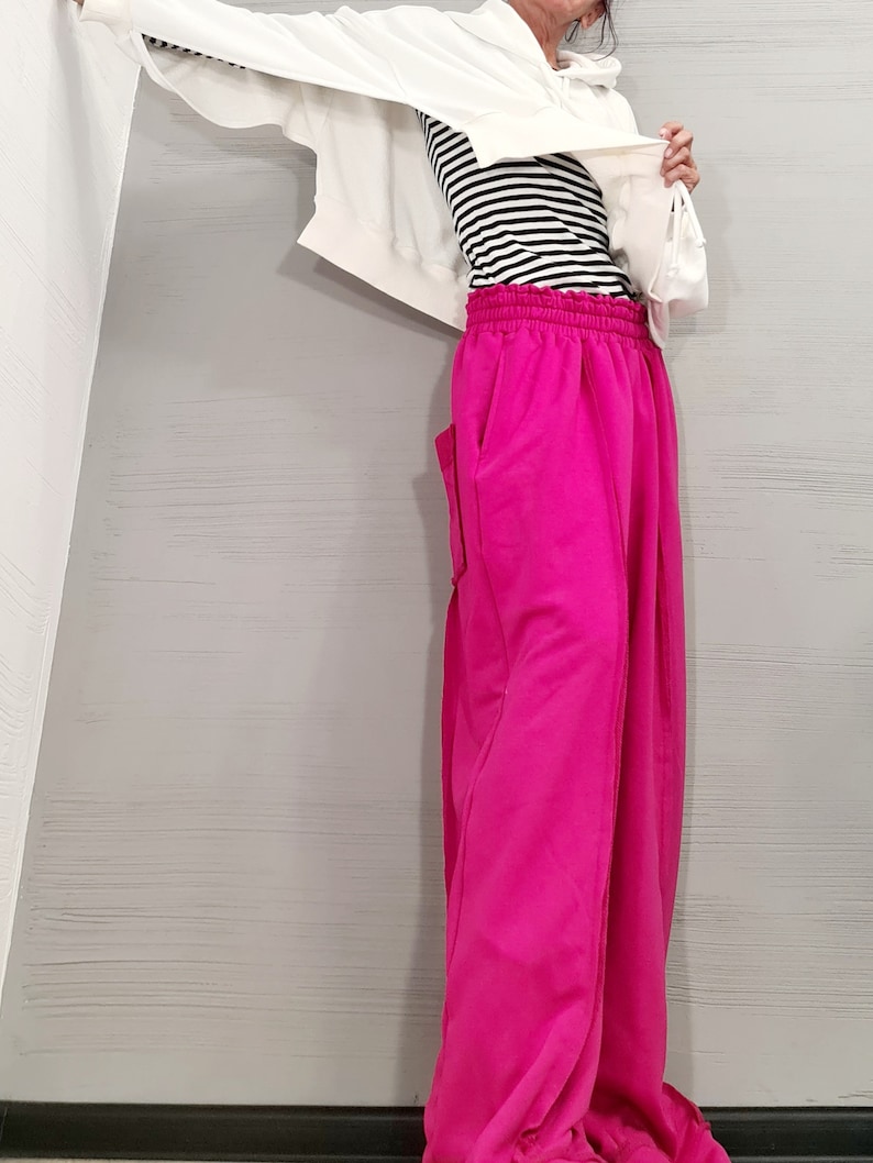 May include: A person wearing a white hooded sweatshirt over a black and white striped top and bright pink sweatpants. The sweatpants have pockets and a drawstring waist. The outfit is casual and comfortable.