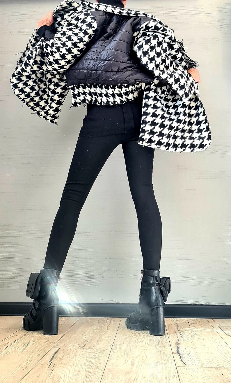 May include: A black and white houndstooth jacket with a black quilted back panel, paired with solid black leggings and black block-heeled ankle boots featuring small attached pouches on the outer sides of the ankles and buckle strap details.
