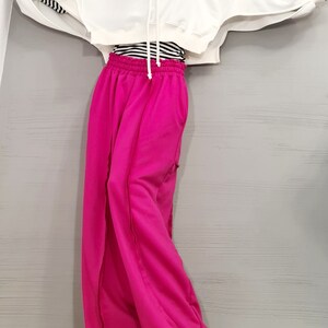 May include: A white cropped hoodie with long sleeves and a drawstring. The sleeves have a black and white striped detail. Paired with bright pink wide-leg sweatpants. A black and white striped shirt is visible underneath the hoodie.