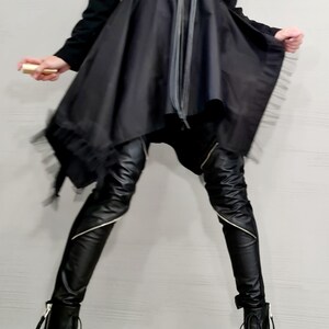 May include: A black outfit featuring a long-sleeved top with an asymmetrical skirt and black leather pants. The outfit is accessorized with a long black necklace and black boots. The pants have silver zippers. The skirt has a tulle trim.