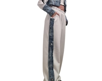 May include: A denim jacket with white sleeves and a matching white crop top and pants. The pants have a denim stripe down the side with snap closures. The outfit is paired with white sneakers.