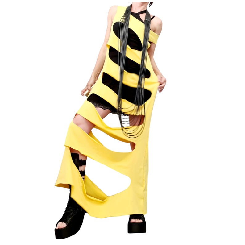 May include: A yellow maxi dress with large cut-out sections and black accents. The dress features a layered design with a black lace trim peeking through the cut-outs. A long black necklace and black platform sandals complete the look.