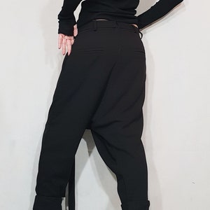 May include: Black outfit featuring a long-sleeved top with an asymmetrical shoulder cut-out and black pants. The pants have a relaxed fit and are paired with black leather ankle boots with zippers.