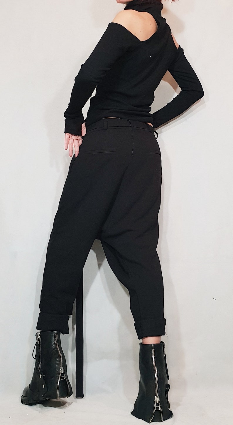 May include: Black outfit featuring a long-sleeved top with an asymmetrical shoulder cut-out and black pants. The pants have a relaxed fit and are paired with black leather ankle boots with zippers.