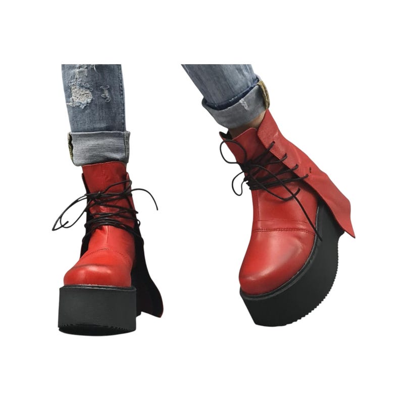 K&ouml;nnte beinhalten: Rote Plateau-Stiefel mit schwarzen Schn&uuml;rsenkeln und schwarzer Sohle. Die Stiefel haben ein einzigartiges Design mit einer Klappe an der Seite. Getragen mit blauen Jeans.