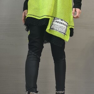 May include: A neon yellow cold-shoulder knit sweater with black long sleeves and a black lace hem, layered over black leggings and black ankle boots featuring silver chain embellishments and side zippers. A white patch with black text is attached.