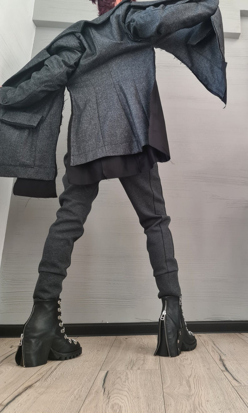 K&ouml;nnte beinhalten: Eine anthrazitfarbene Jacke mit Lagen-Design und schwarzen Stoffeins&auml;tzen, kombiniert mit einer passenden, schmal geschnittenen anthrazitfarbenen Hose mit gerippten B&uuml;ndchen. Das Outfit wird durch schwarze Lederstiefeletten mit silbernen Rei&szlig;verschl&uuml;ssen abgerundet.