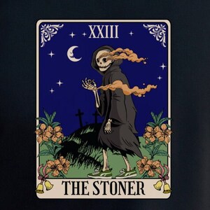May include: Black t-shirt featuring a tarot card design. The card depicts a skeletal figure in a black cloak, with the text "THE STONER" at the bottom. The background shows a night sky with a crescent moon and stars.