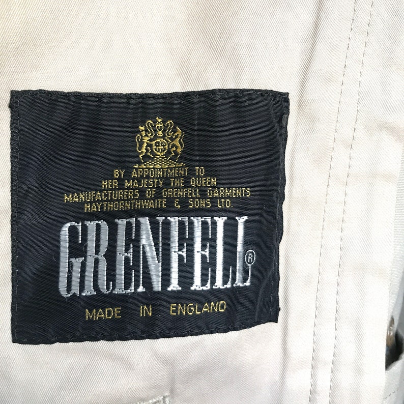 K&ouml;nnte beinhalten: Ein schwarzes Etikett mit goldenen Buchstaben, auf dem steht "By Appointment to Her Majesty the Queen Manufacturers of Grenfell Garments Haythornthwaite & Sons Ltd. Grenfell Made in England".