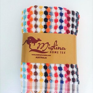 May include: A colorful, folded towel with a textured, dotted pattern in white, orange, red, yellow, black, blue, and pink. The towel has a fringed edge and a brown paper band with the text "Mislina Home Tex Australia".