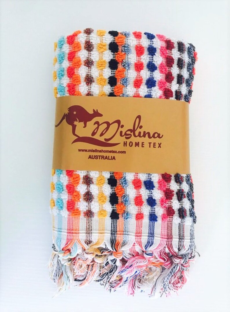 May include: A colorful, folded towel with a textured, dotted pattern in white, orange, red, yellow, black, blue, and pink. The towel has a fringed edge and a brown paper band with the text "Mislina Home Tex Australia".