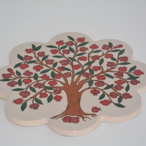 Puede incluir: Un salvamanteles decorativo de cerámica con un diseño floral. El salvamanteles tiene forma de flor con fondo beige. En el centro hay un árbol marrón con granadas rojas y hojas verdes. El salvamanteles mide aproximadamente 18 cm de diámetro.