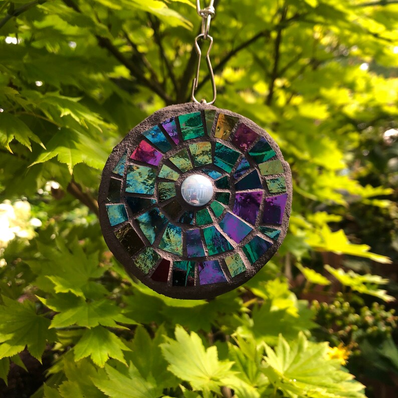 K&ouml;nnte beinhalten: Ein runder, schillernder Mosaik-Sonnenf&auml;nger mit dunkelgrauem Hintergrund und einem silbernen, reflektierenden Zentrum. Der Sonnenf&auml;nger h&auml;ngt an einer silbernen Kette.
