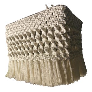 Puede incluir: Una pantalla de lámpara de macramé blanca con un borde de flecos. La pantalla de la lámpara está hecha de un cordón grueso y tejido y tiene una forma cuadrada.