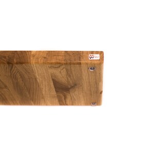 May include: A rectangular wooden cutting board with a natural wood grain pattern. The board has a light brown color and is made of end-grain wood. The "Magical Wood" logo is visible on the top right corner. Metal screws are visible on the bottom.