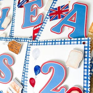 May include: A collection of decorative paper cutouts with a British theme. The cutouts include the letters "H E A S 2", a Union Jack flag, a red double-decker bus, Big Ben, and various food and balloon illustrations. The letters are blue with red trim.