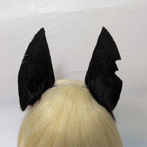May include: Black bat ears headband. The headband is made of soft, black fabric and is designed to look like bat ears. The headband is worn on a person's head.