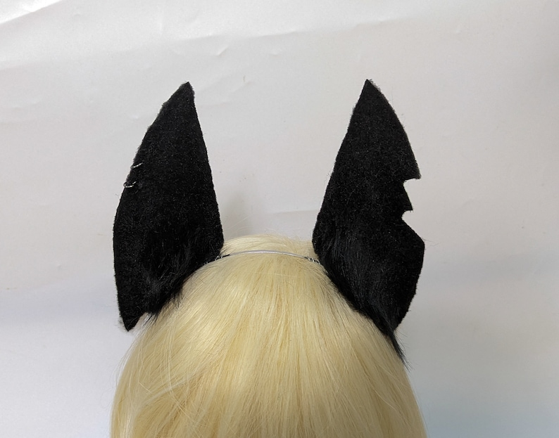 May include: Black bat ears headband. The headband is made of soft, black fabric and is designed to look like bat ears. The headband is worn on a person's head.