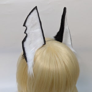 May include: A pair of black and white faux fur ears with a black felt backing. The ears are attached to a headband.