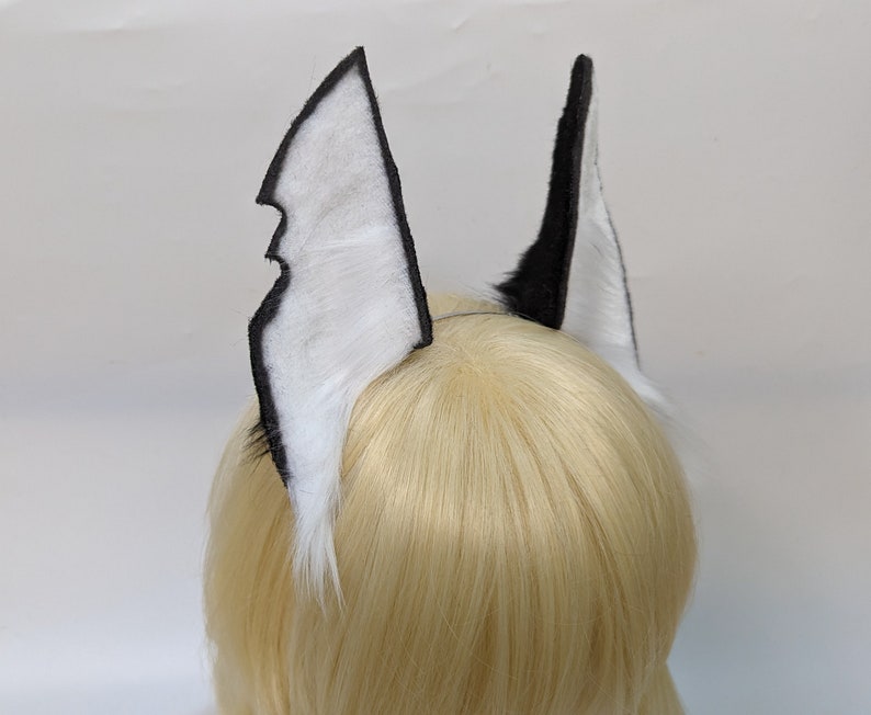 May include: A pair of black and white faux fur ears with a black felt backing. The ears are attached to a headband.