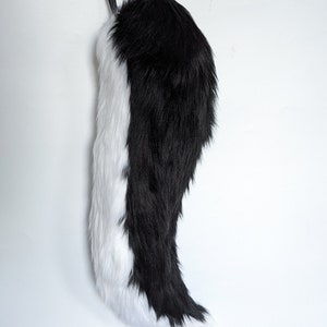 May include: A black and white faux fur tail with a black ribbon attached to the top.