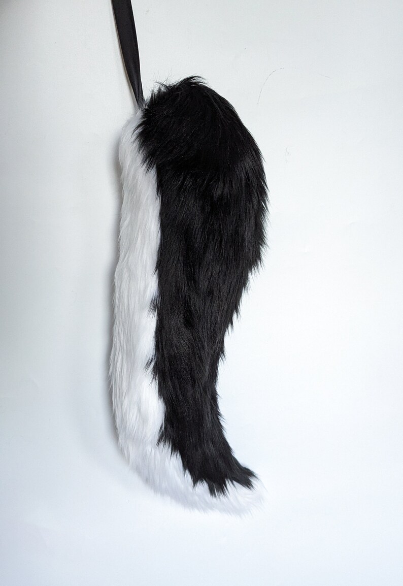 May include: A black and white faux fur tail with a black ribbon attached to the top.