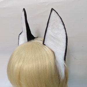 May include: A pair of black and white faux fur cat ears with a black headband. The ears are made of soft, fluffy fur and are attached to a black headband.